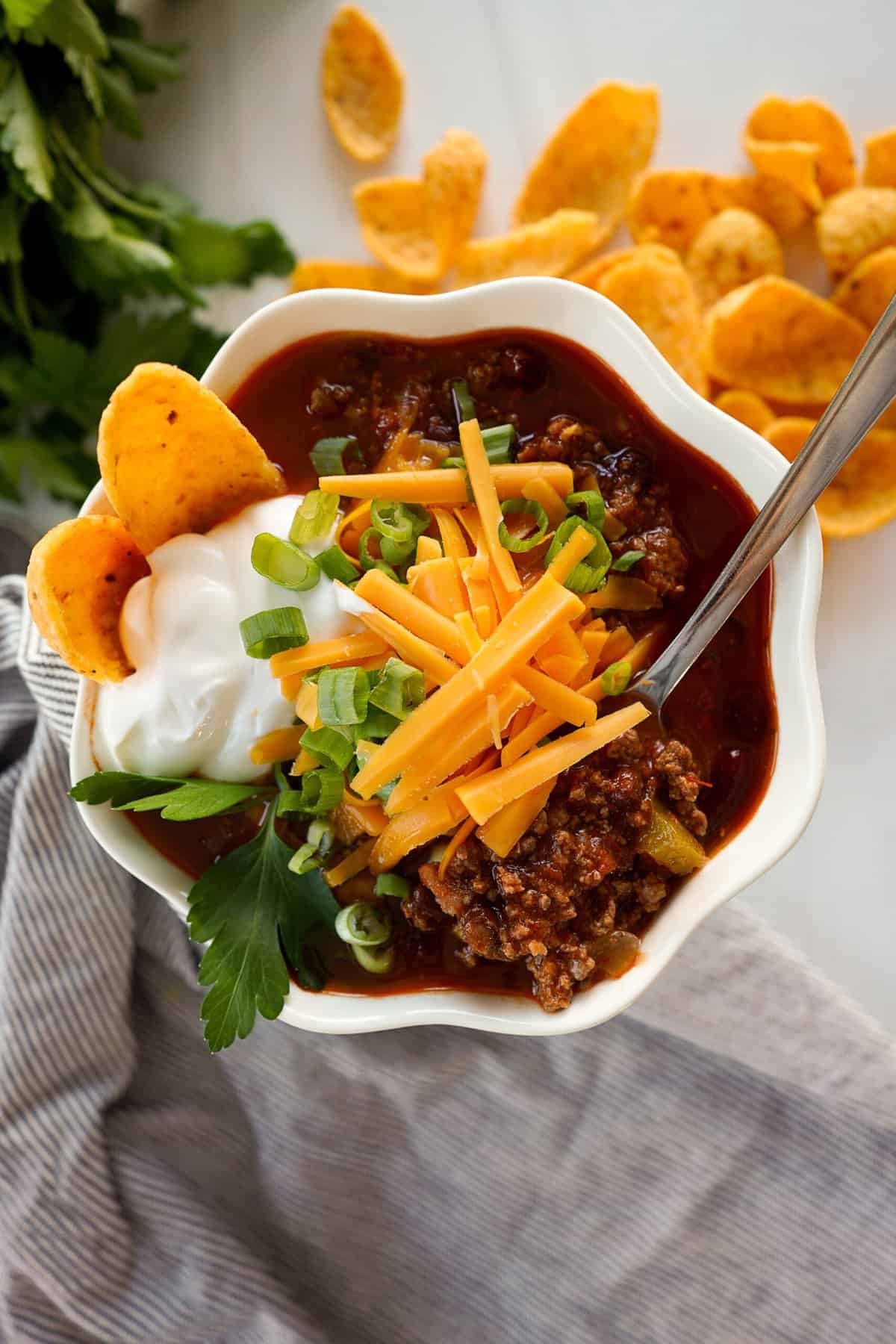 bowl of chili with sour cream, cheese, green onions and corn chips