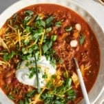 A bowl of slow cooker chili with sour cream, green onion, and cheese.
