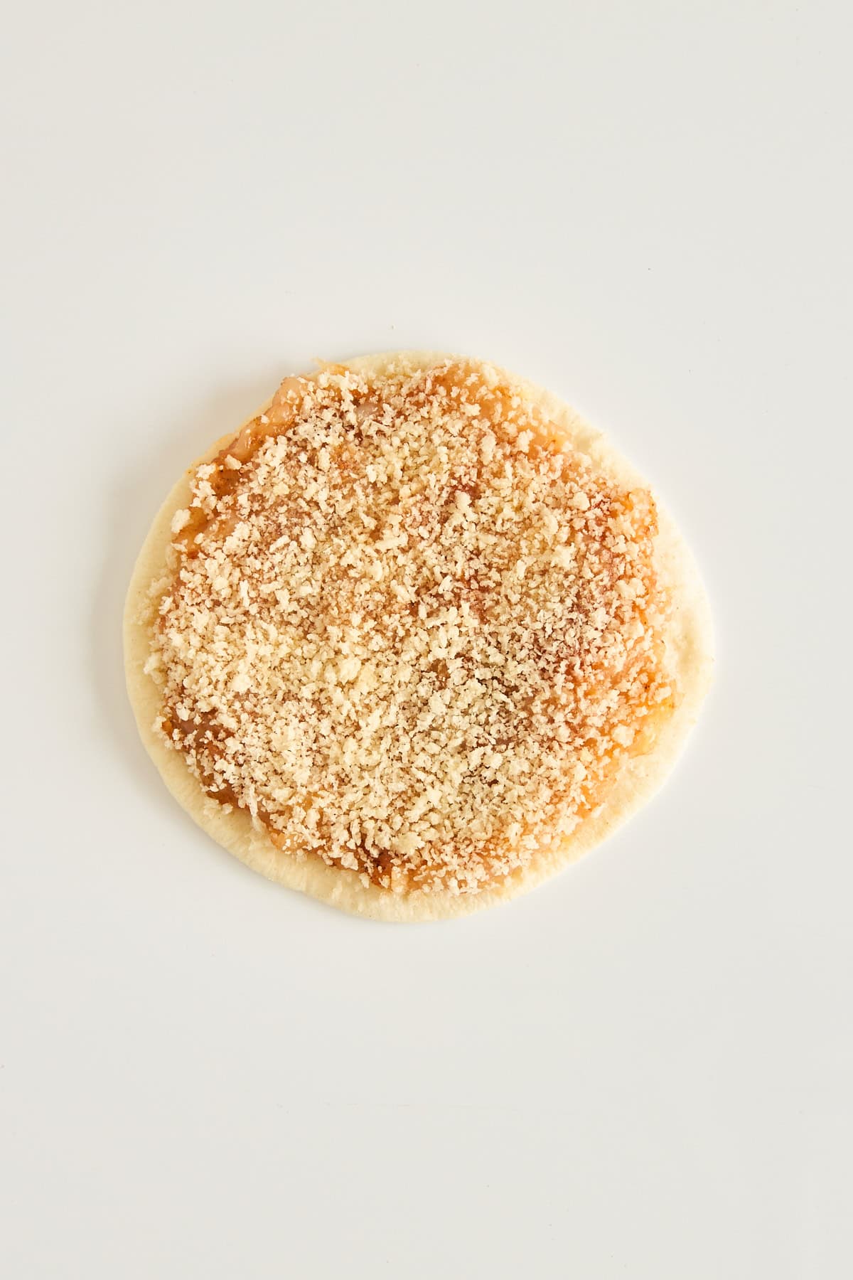 A round piece of dough topped with a crumbly brown sugar and cinnamon mixture, placed on a plain white background.