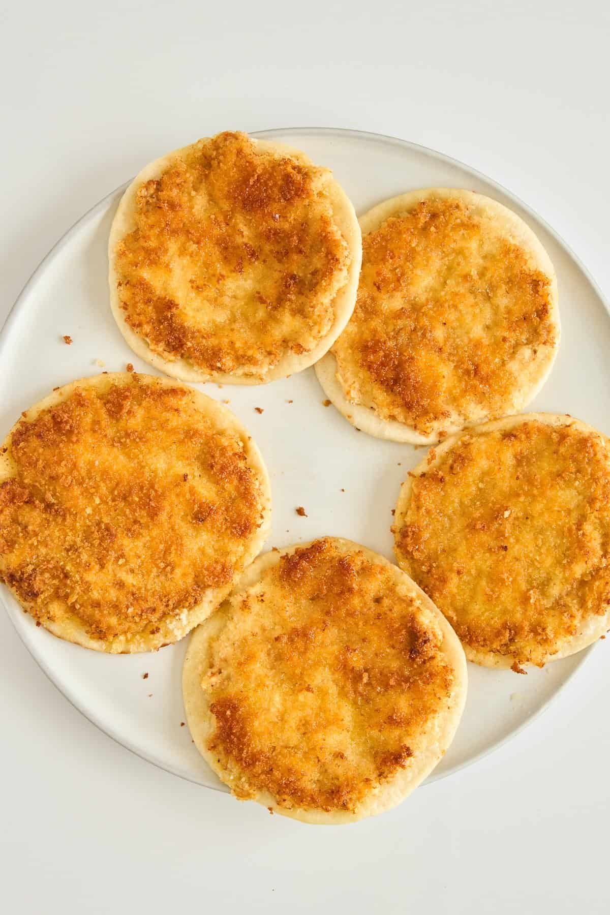 A plate with five round flatbreads topped with a golden, crispy layer, arranged in a circular pattern on a white background.