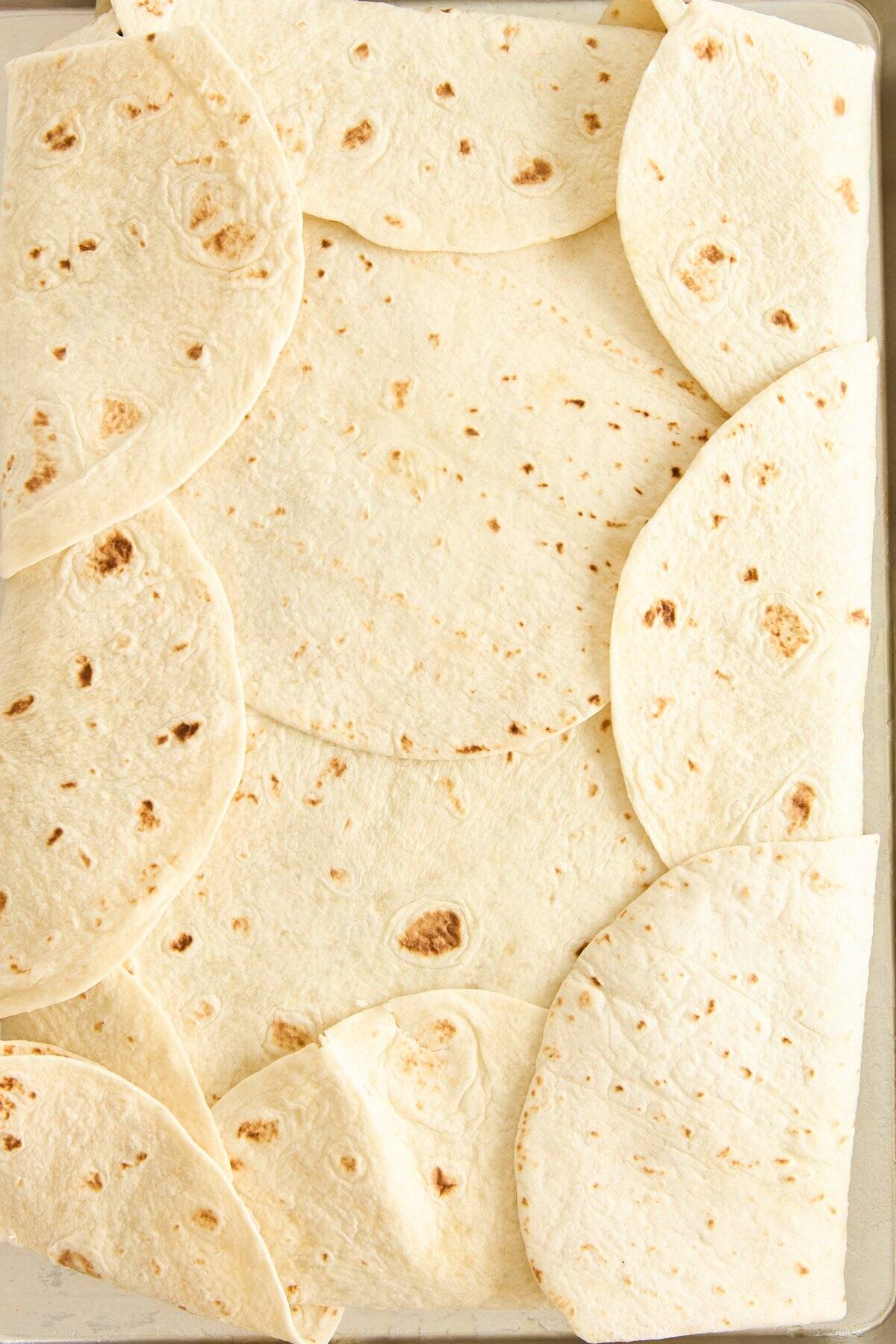 A rectangular baking dish lined with overlapping flour tortillas, covering the bottom and sides.
