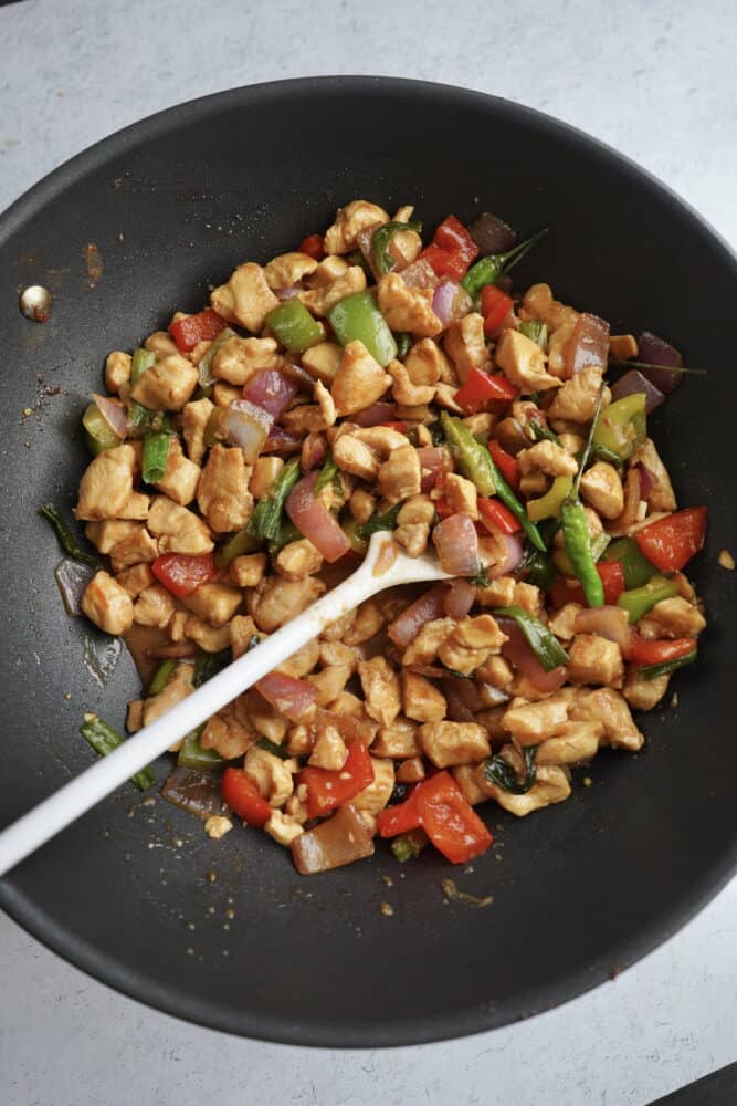 overhead image of a wok with kung pao chicken being stirred with a spoon