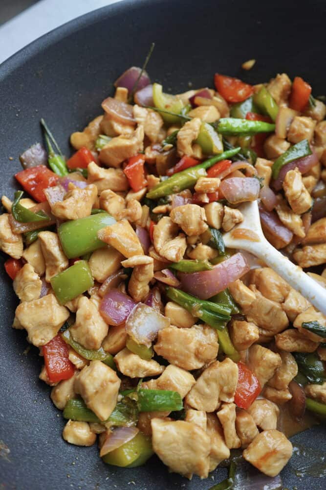 a wooden spoon stirring kung pao chicken in a wok 