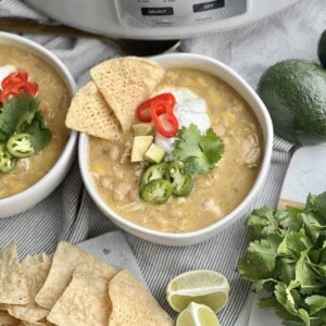 a bowl of slow cooker white chicken chili topped with jalapenos, sour cream, avocado, and tortilla chips