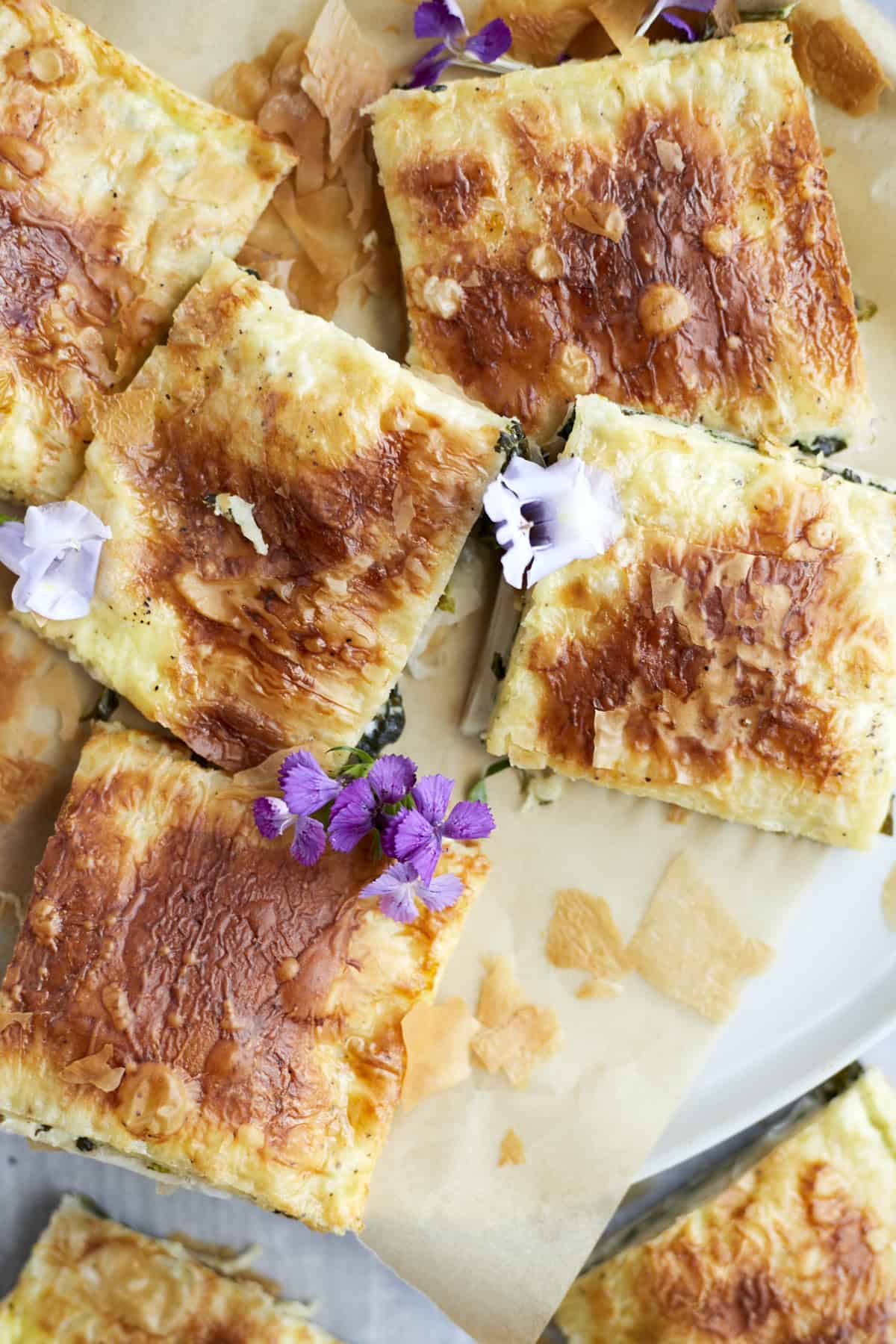 squares of baked phyllo spinach pie on parchment paper