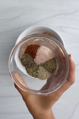 a woman's hand holding a glass bowl full of spices