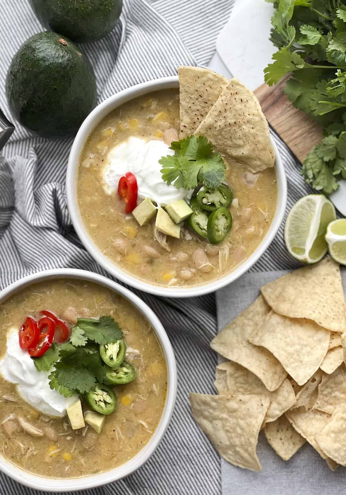 two bowls of white chicken chili with sour cream, avocado, jalapeño, and tortilla chips.