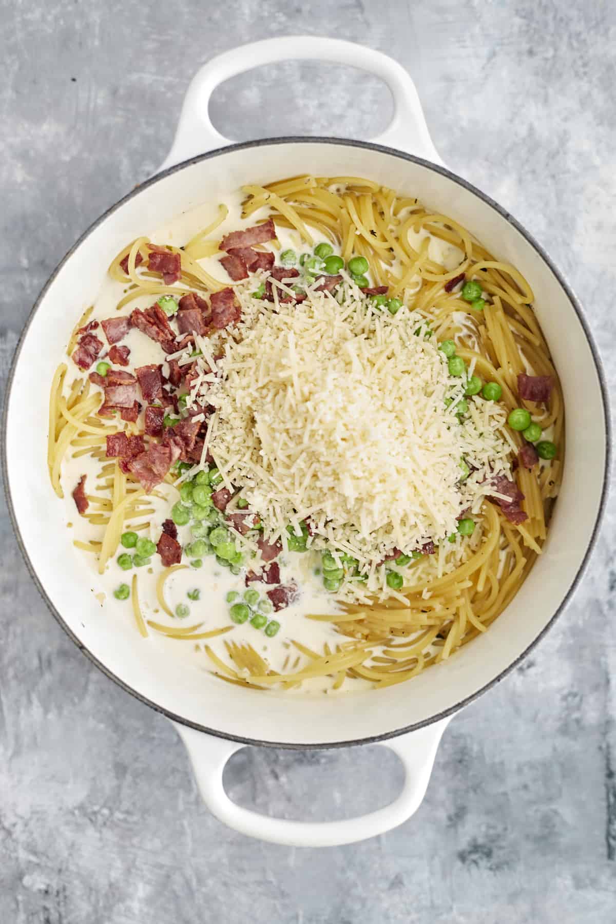 cooked spaghetti noodles, bacon, peas, cream, and Parmesan in a pot to make spaghetti carbonara