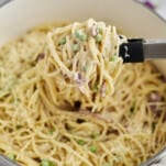 overhead image of spaghetti carbonara in a white pot with a serving being lifted with tongs