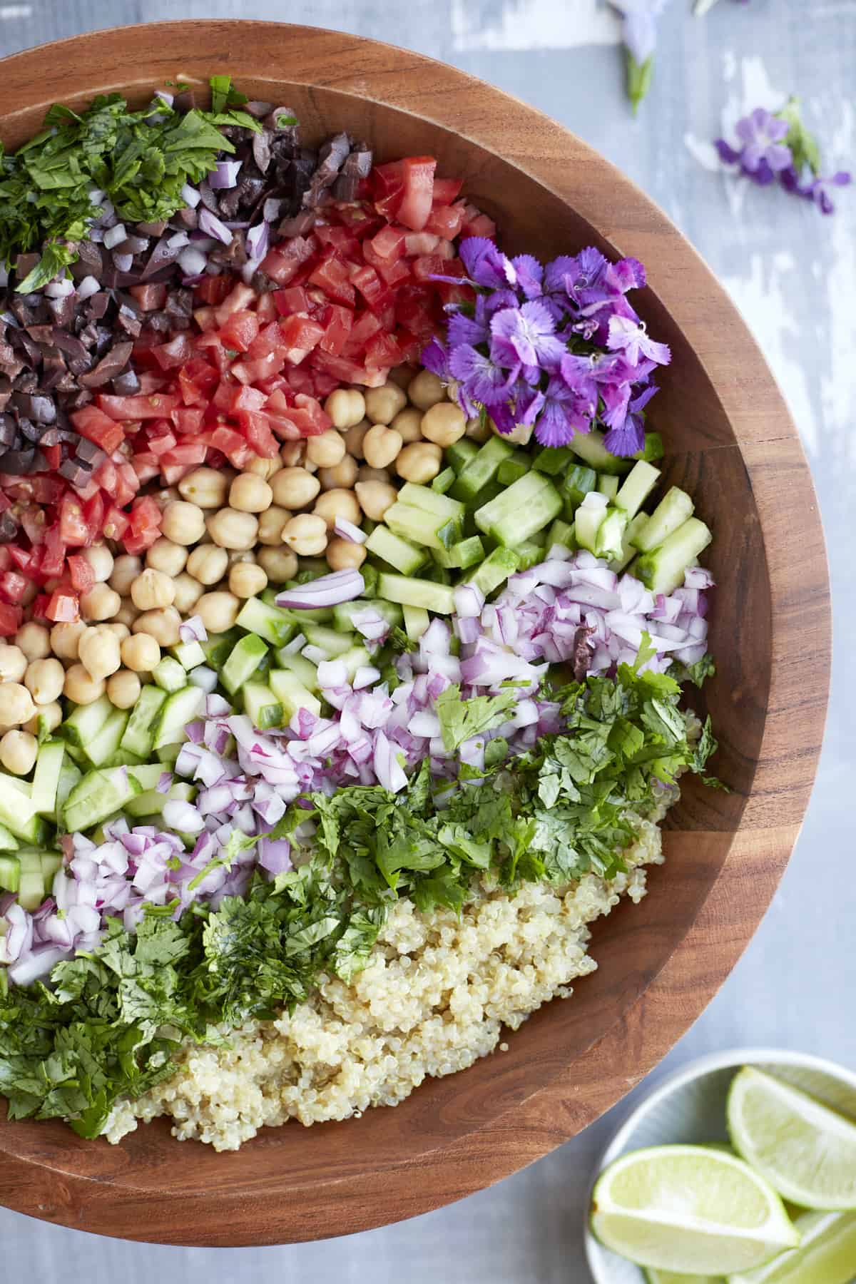 overhead image of a Mediterranean Quinoa Salad in a brown bowl with a small white bowl of lime wedges on the side