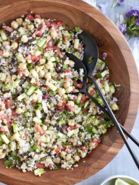 Mixed up Mediterranean Quinoa Salad in a large wooden bowl with serving spoons on the side