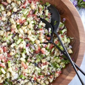 Mixed up Mediterranean Quinoa Salad in a large wooden bowl with serving spoons on the side