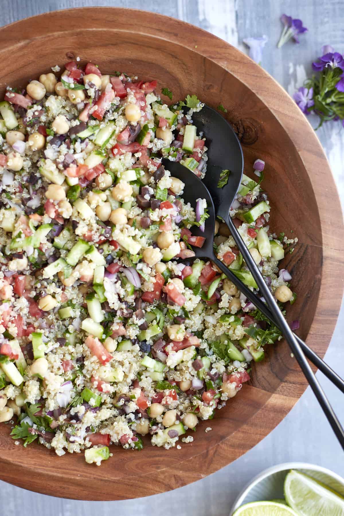 Mediterranean Quinoa Salad mixed up in a wooden bowl with serving spoons on the side