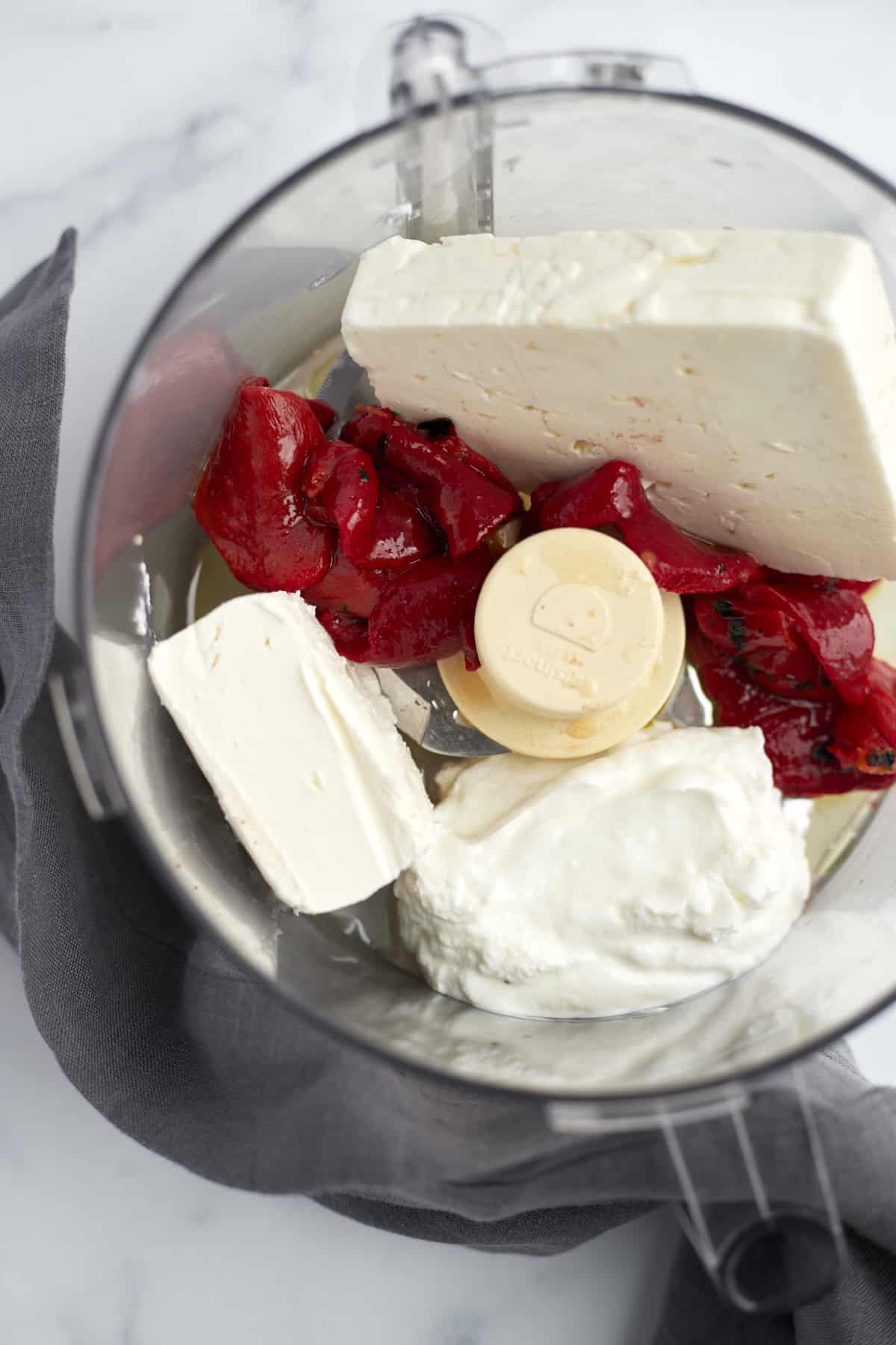 blocks of feta, roasted red peppers, and Greek yogurt in a food processor 