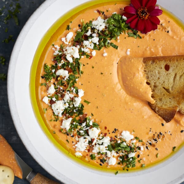 A bowl of roasted red pepper feta dip with a piece of bread sticking out.
