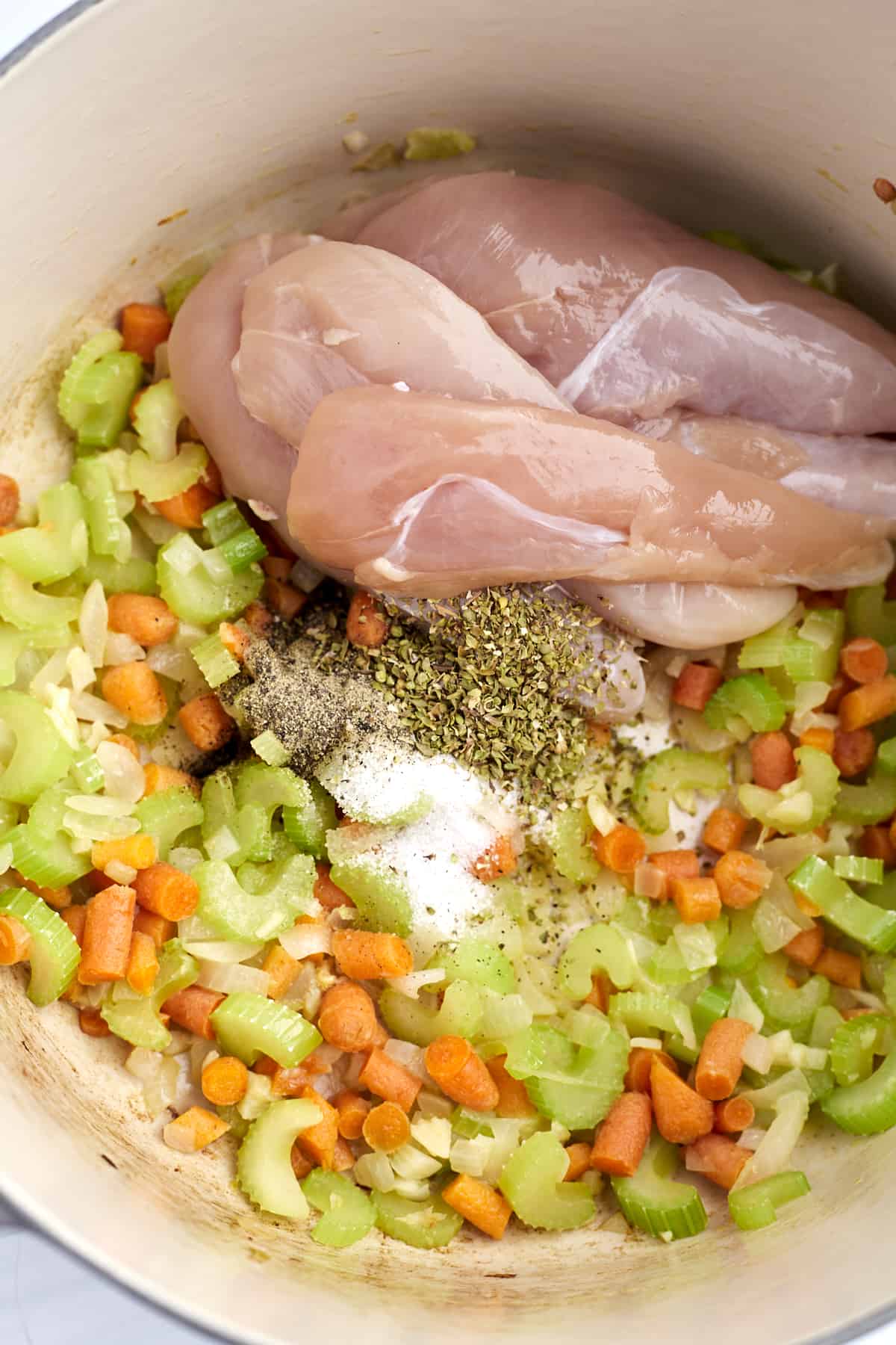 overhead of dutch oven with chicken, herbs, celery, carrots, and onions
