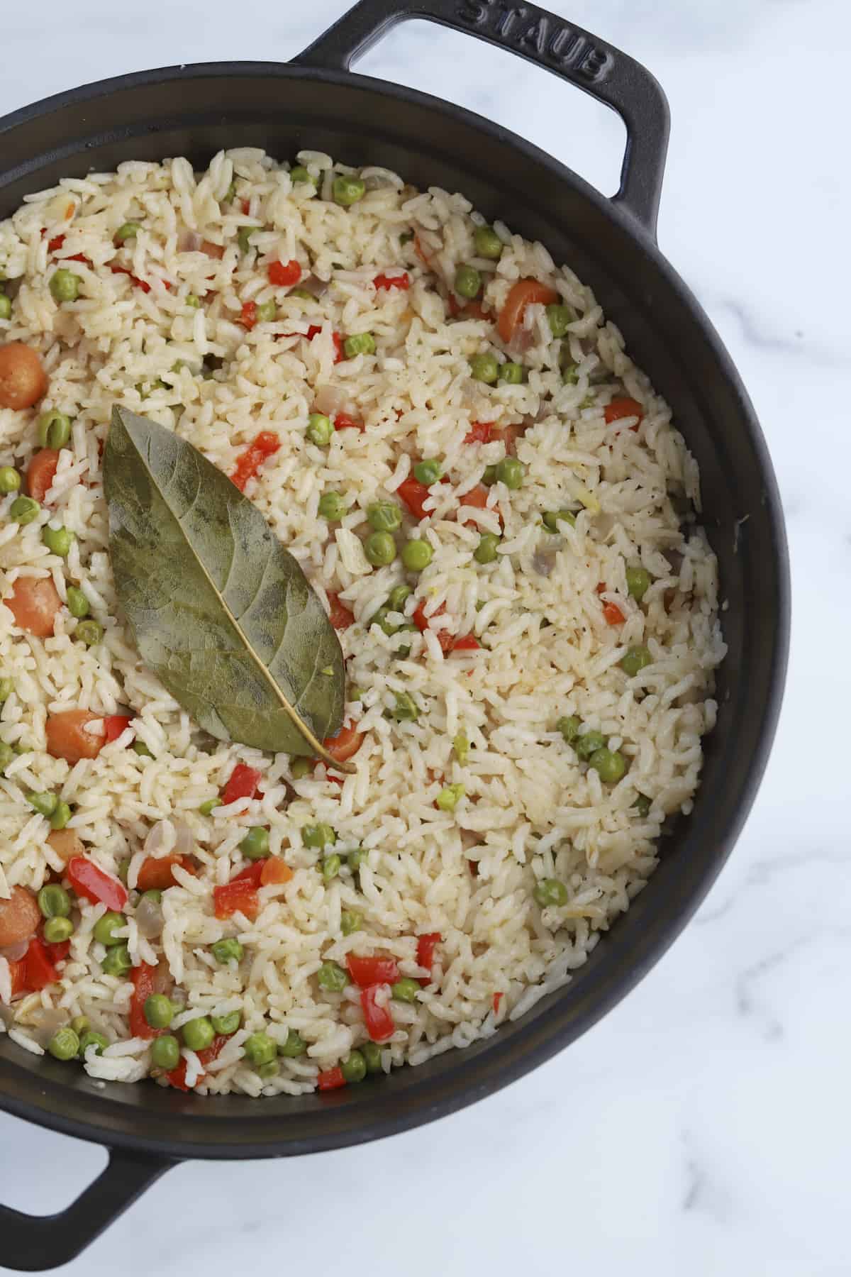 overhead of veggie rice with bayleaf in a cast iron pan