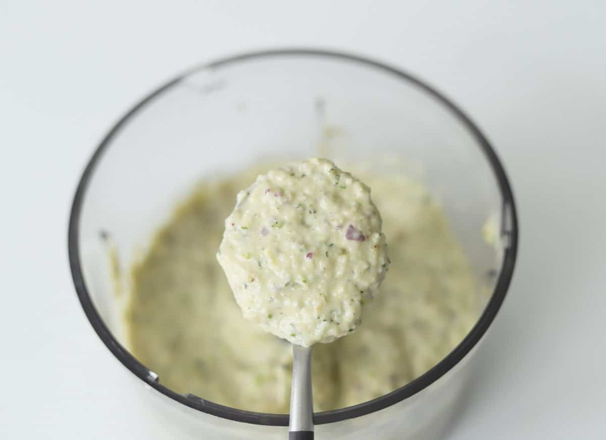 A spoonful of green goddess salad dressing over a food processor. 