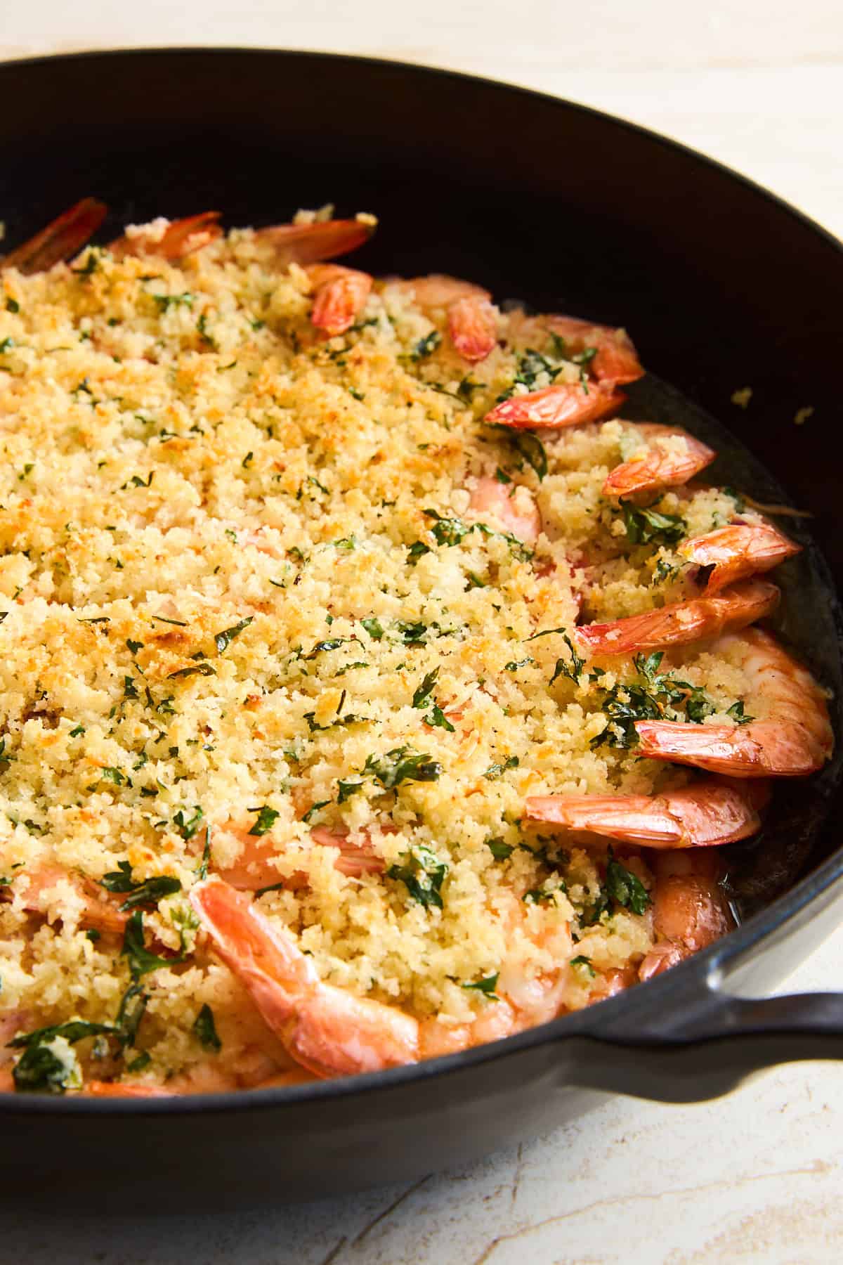 Shrimp baked in a black skillet, topped with golden, crispy breadcrumbs mixed with herbs. The shrimp are arranged in a circular pattern along the edge of the pan.