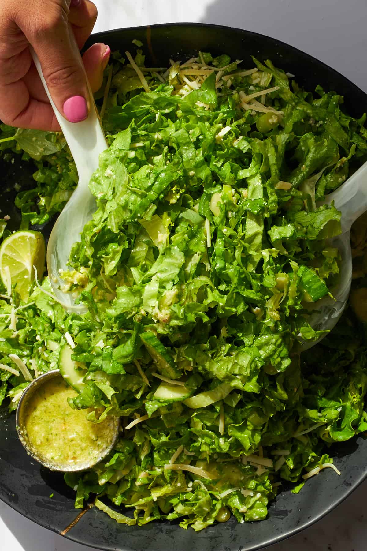 Green goddess salad being tossed with dressing on the side. 