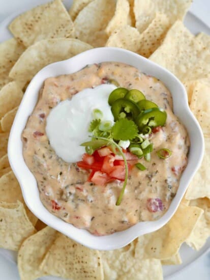 overhead image of homemade queso fundido dip in a white bowl surrounded by tortilla chips