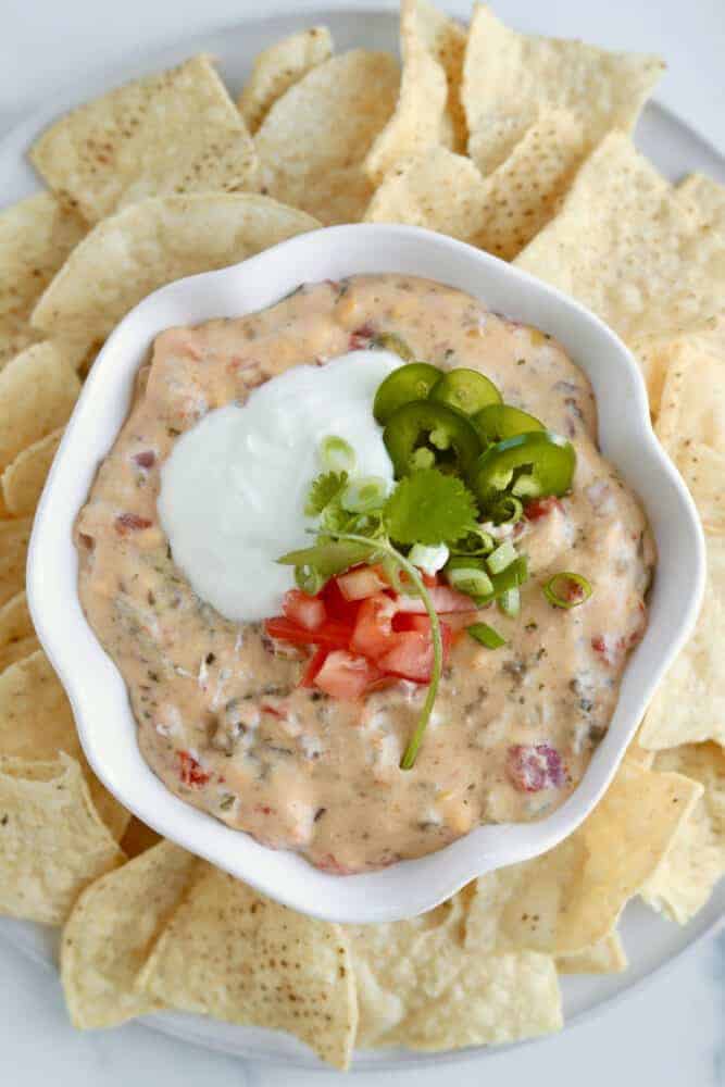 overhead image of homemade queso fundido dip in a white bowl surrounded by tortilla chips