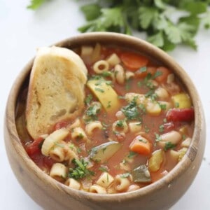 a bowl of minestrone soup with crostini dipped in