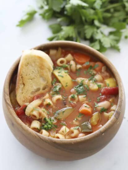 a bowl of minestrone soup with crostini dipped in