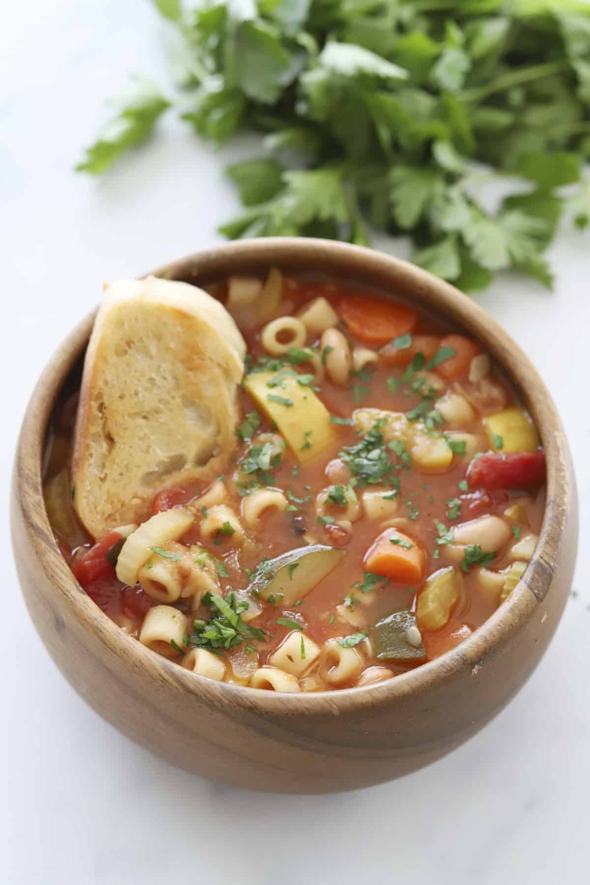 a bowl of minestrone soup with a piece of crostini dipped in 
