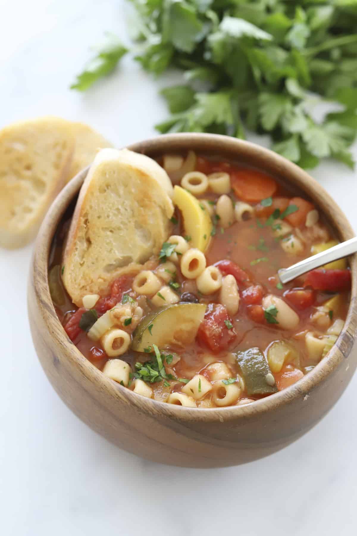 a bowl of minestrone soup with a spoon sticking out and toasted crostini dipped in 