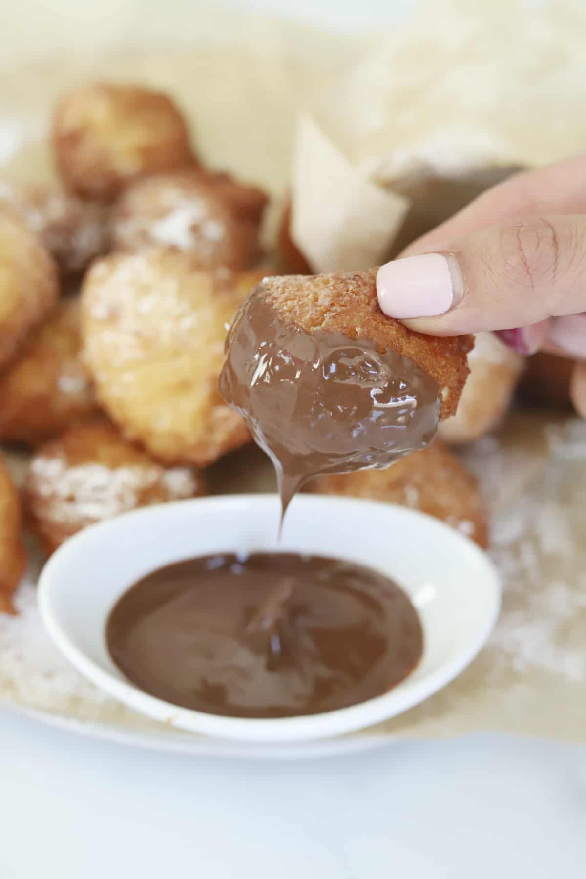 A Zeppole being dipped in melted Nutella. 