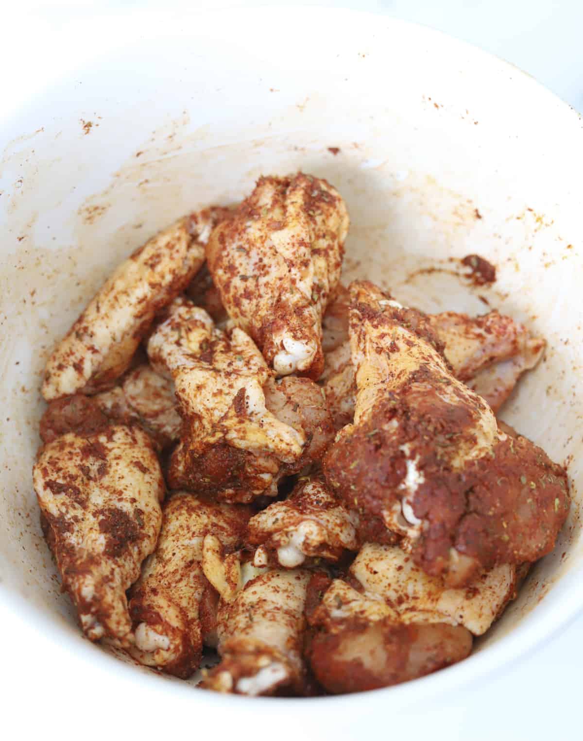 raw chicken wings in a bowl coated with spices