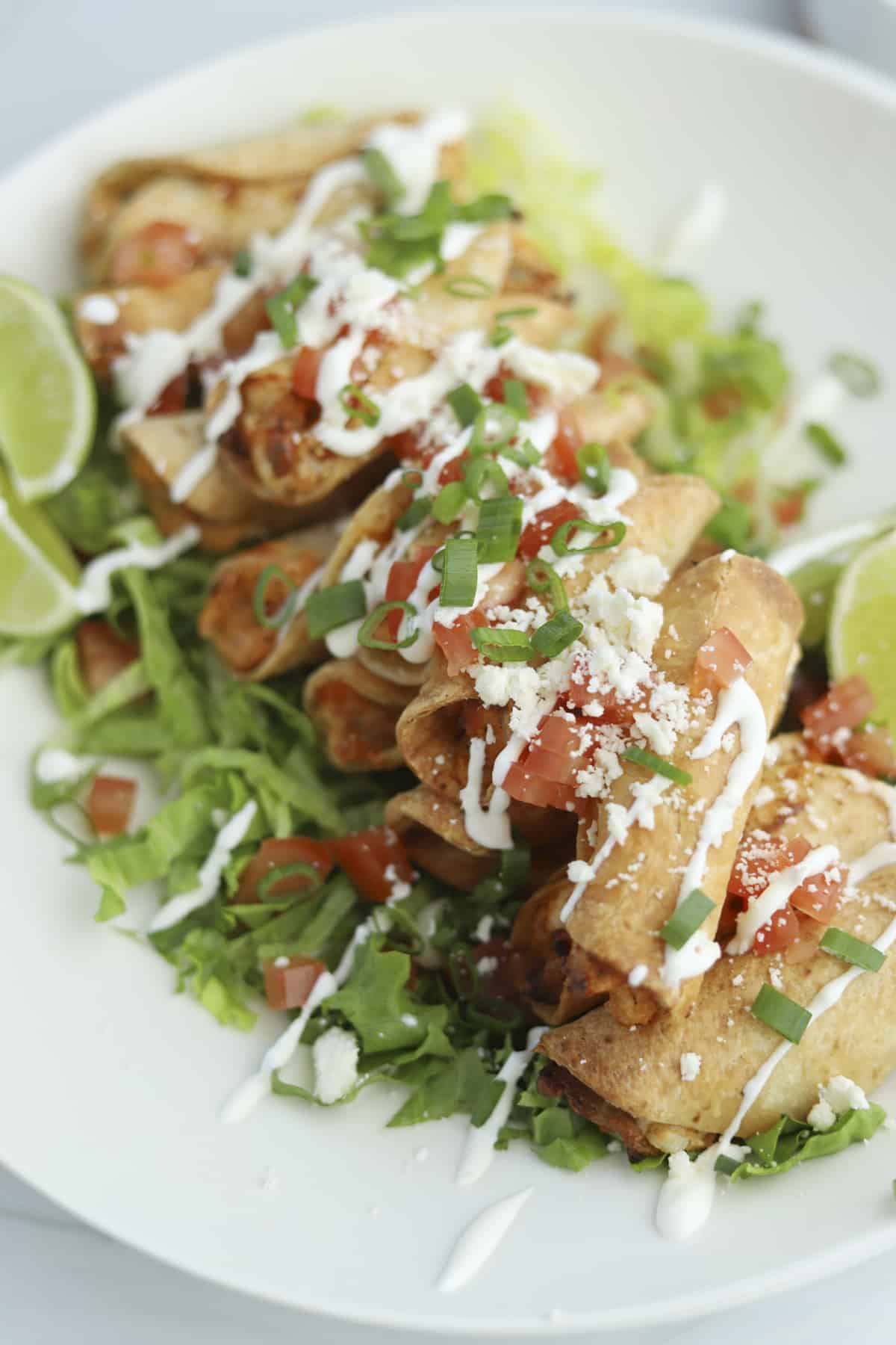 overhead of mini air fryer taquitos with tomatoes, sour cream, and green onions