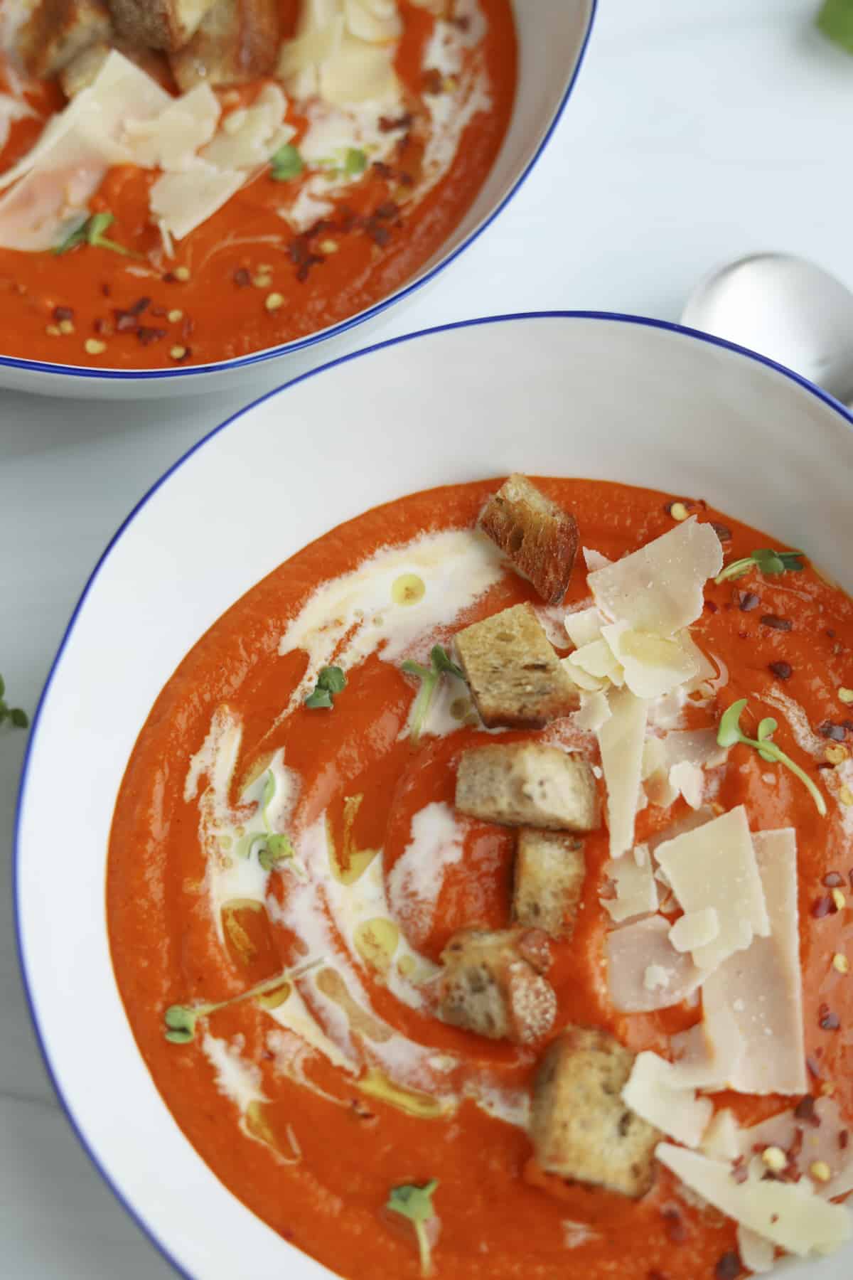 two bowls of roasted red pepper and cauliflower soup topped with croutons and Parmesan
