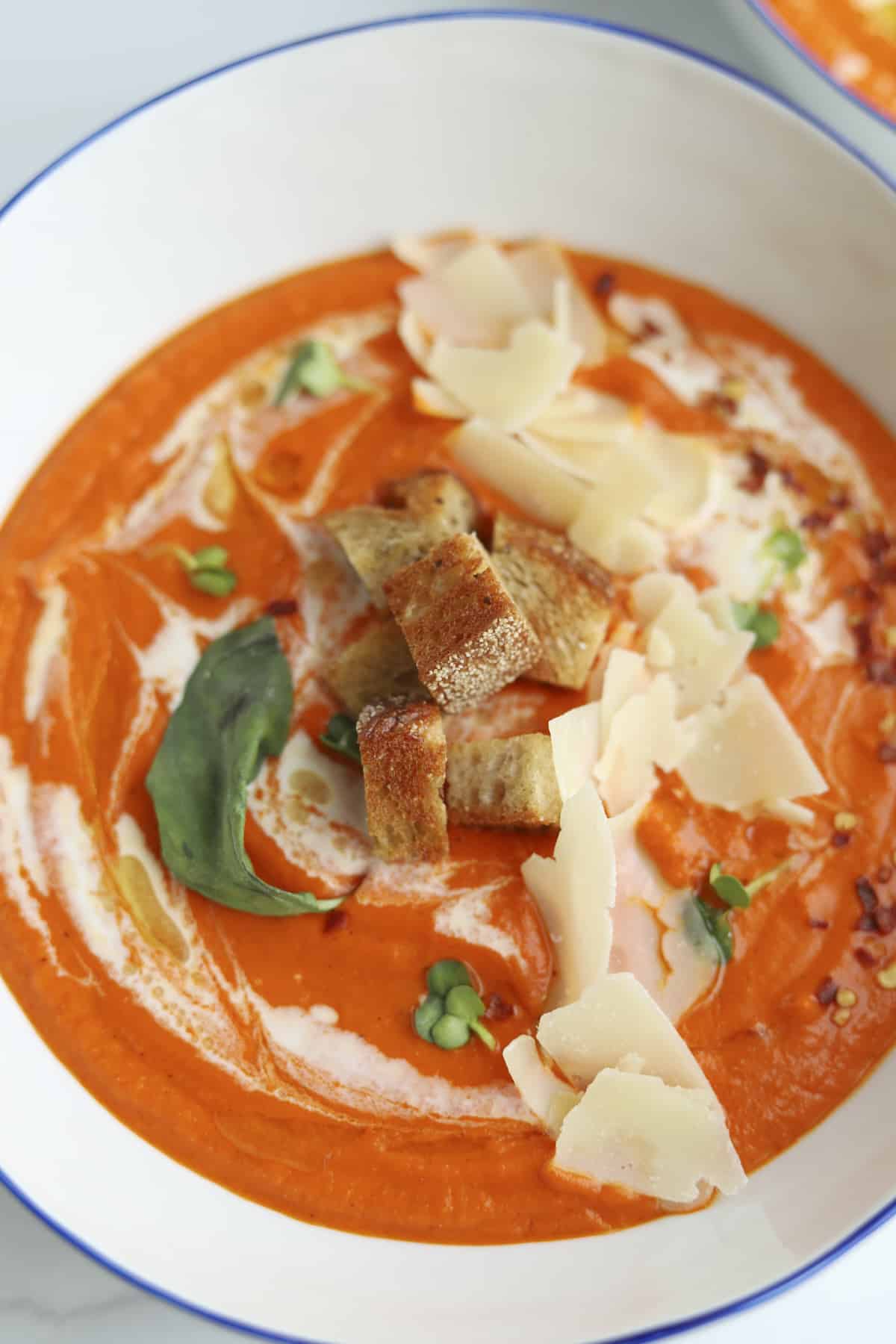 a bowl of roasted red pepper and cauliflower soup topped with croutons and Parmesan flakes