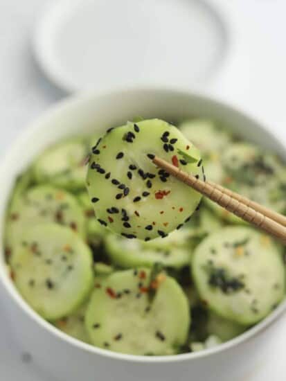 a bowl of Asian cucumber salad with a cucumber slice being held with chopsticks.