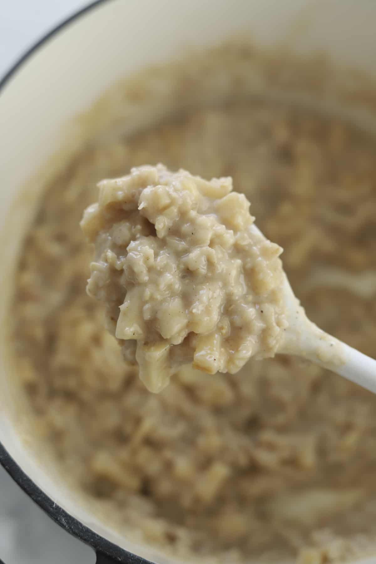 a wooden spoon scooping up apple cinnamon oatmeal from a pot 