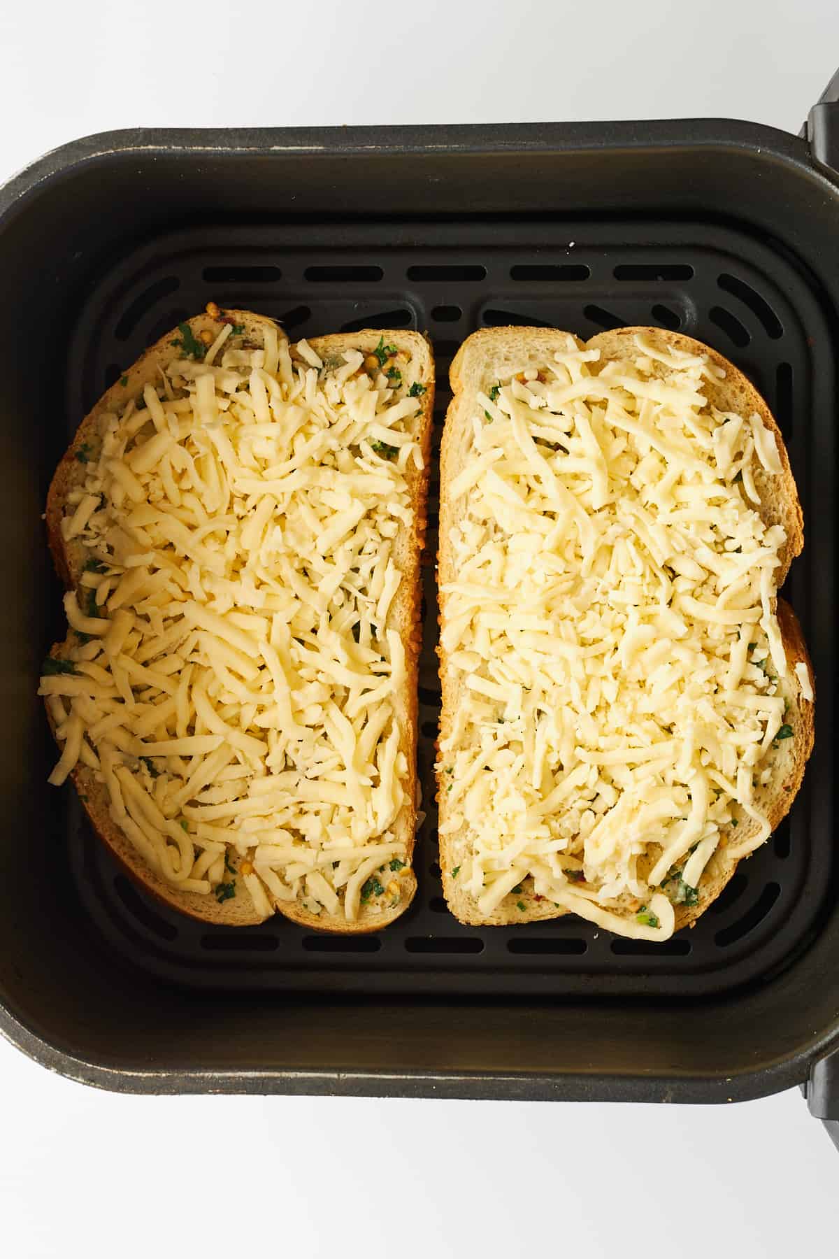 Two pieces of air fryer cheesy garlic toast in an air fryer basket. 