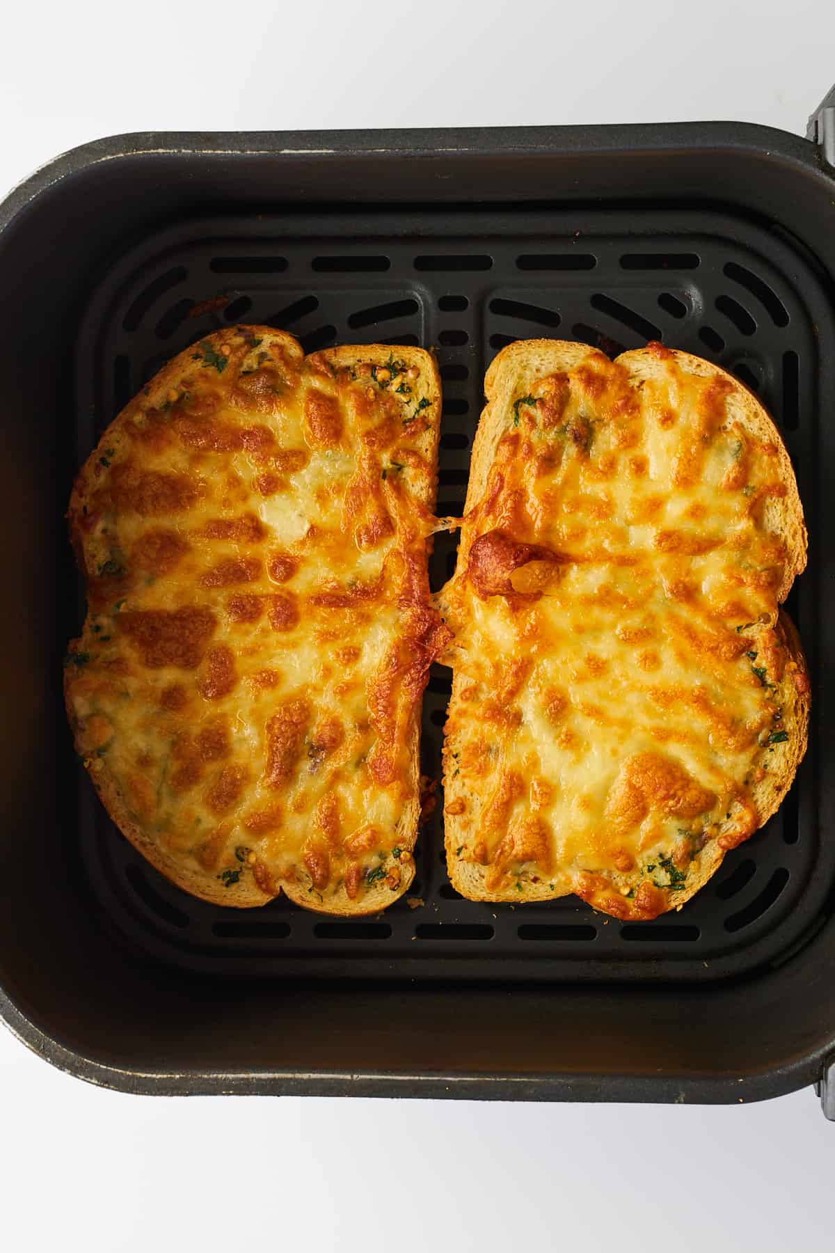 Two cooked cheesy garlic toast slices in an air fryer basket. 
