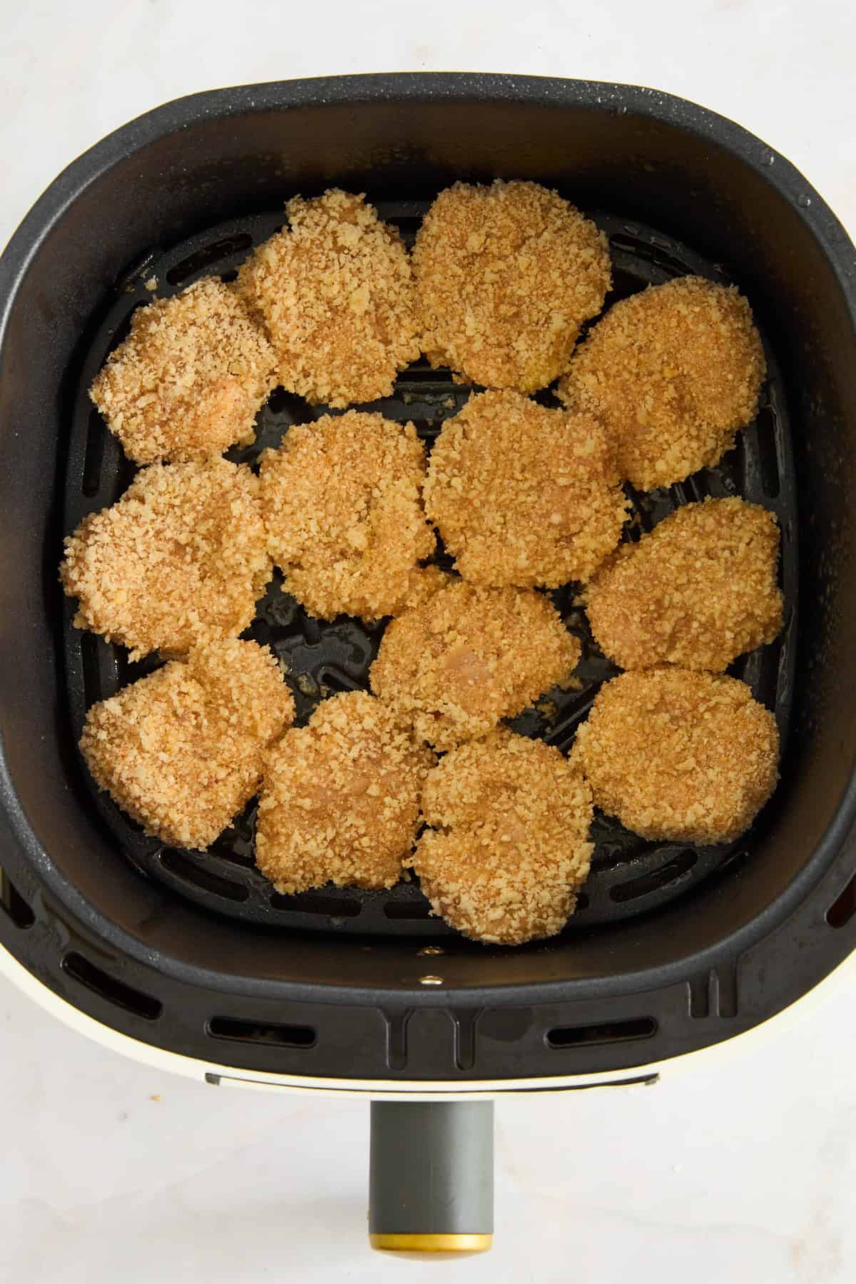Raw chicken nuggets in an air fryer basket.