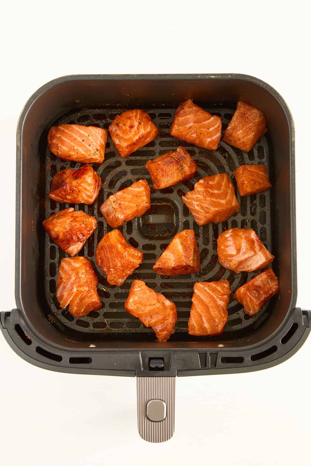 Raw seasoned salmon pieces in an air fryer basket.