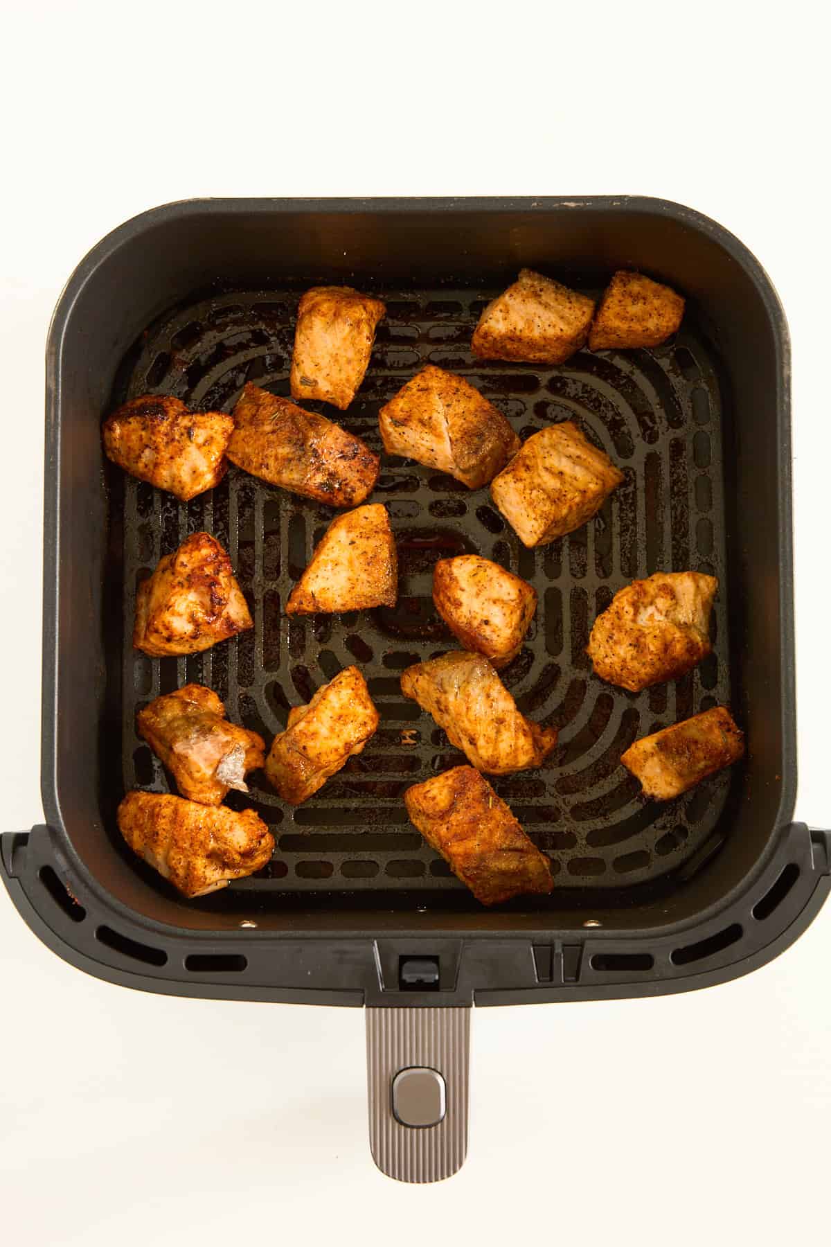 Cooked salmon bites in an air fryer basket.