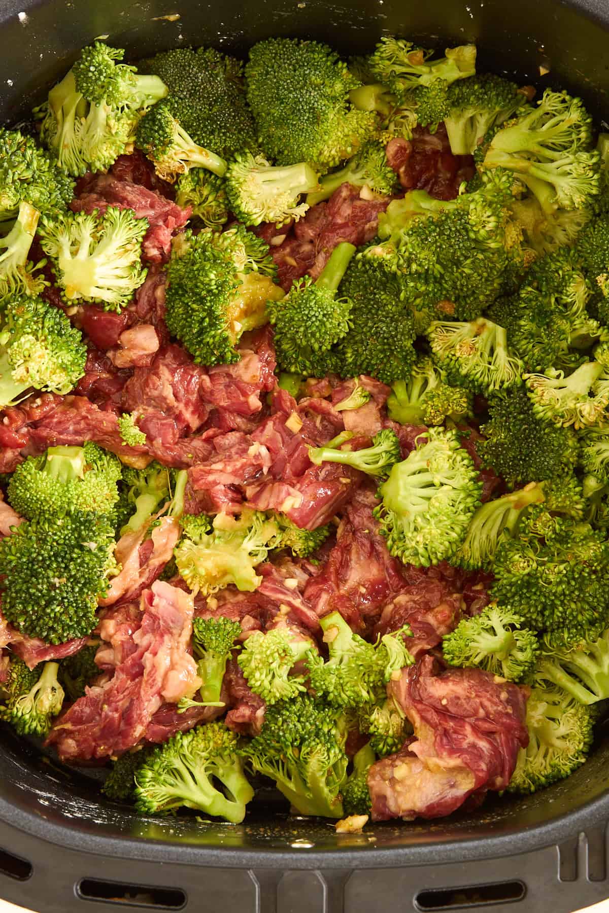 Raw air fryer beef and broccoli in an air fryer basket.
