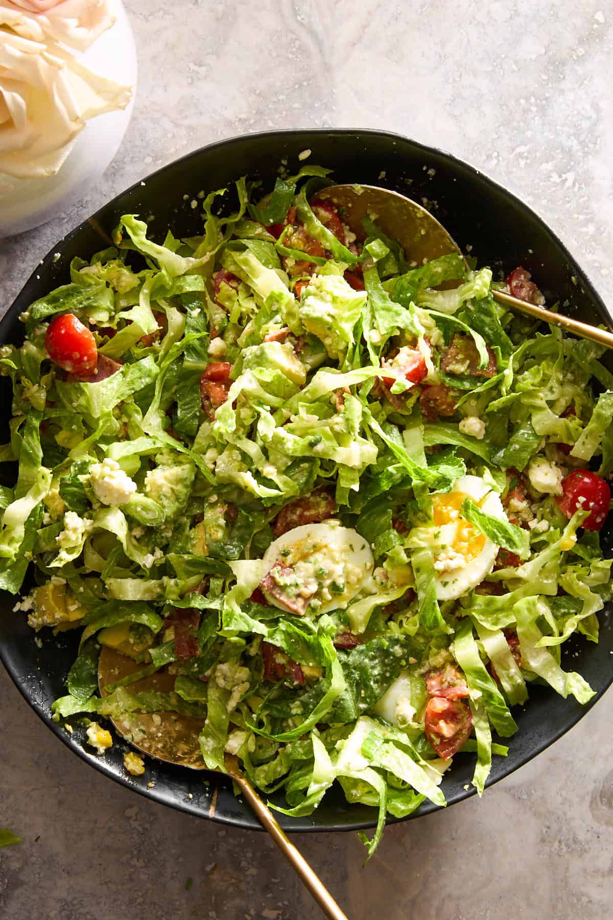 A Cobb salad being tossed with green goddess dressing. 