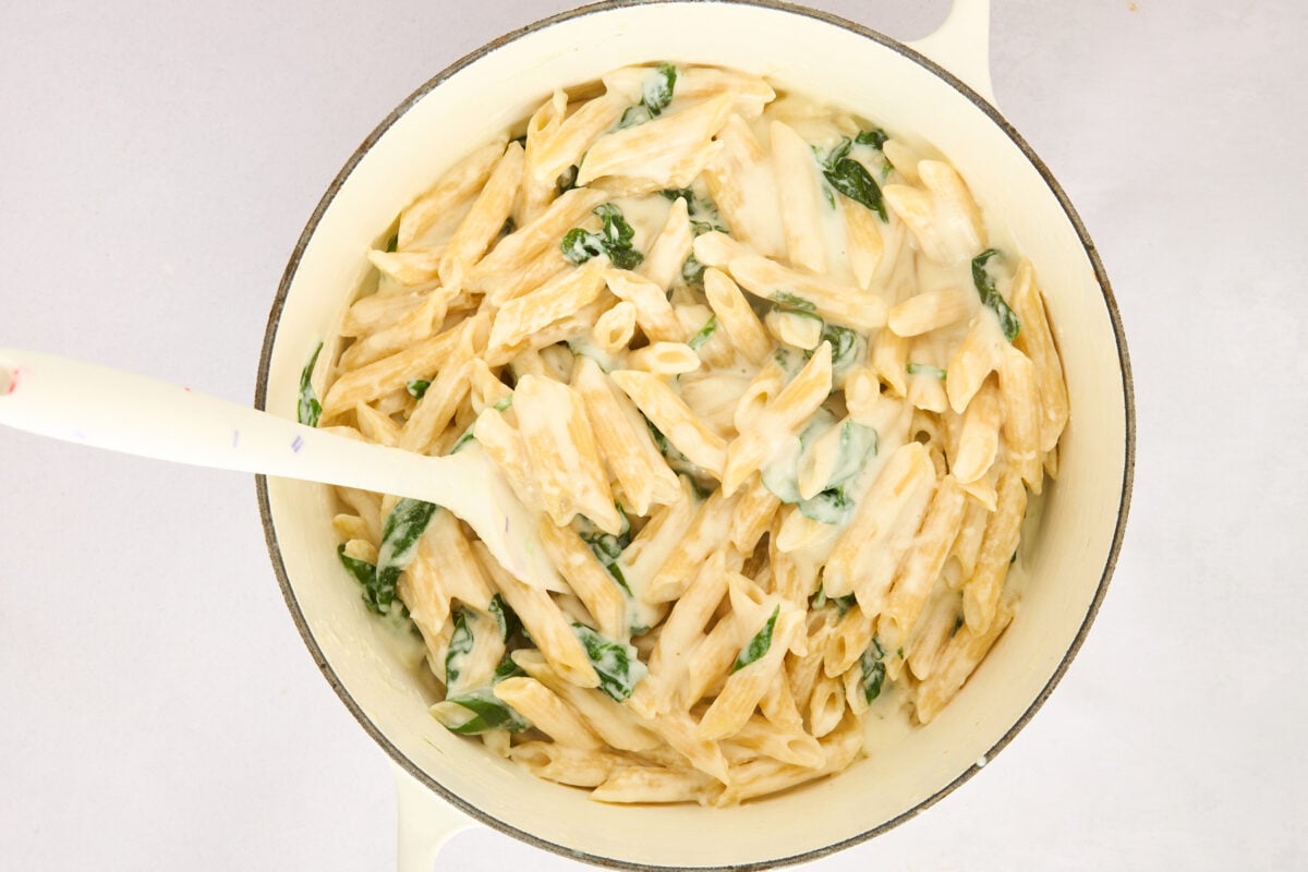 Penne pasta being tossed with cottage cheese sauce and spinach in a pot.