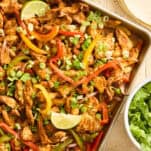 Sheet pan chicken fajitas topped with lime wedges.