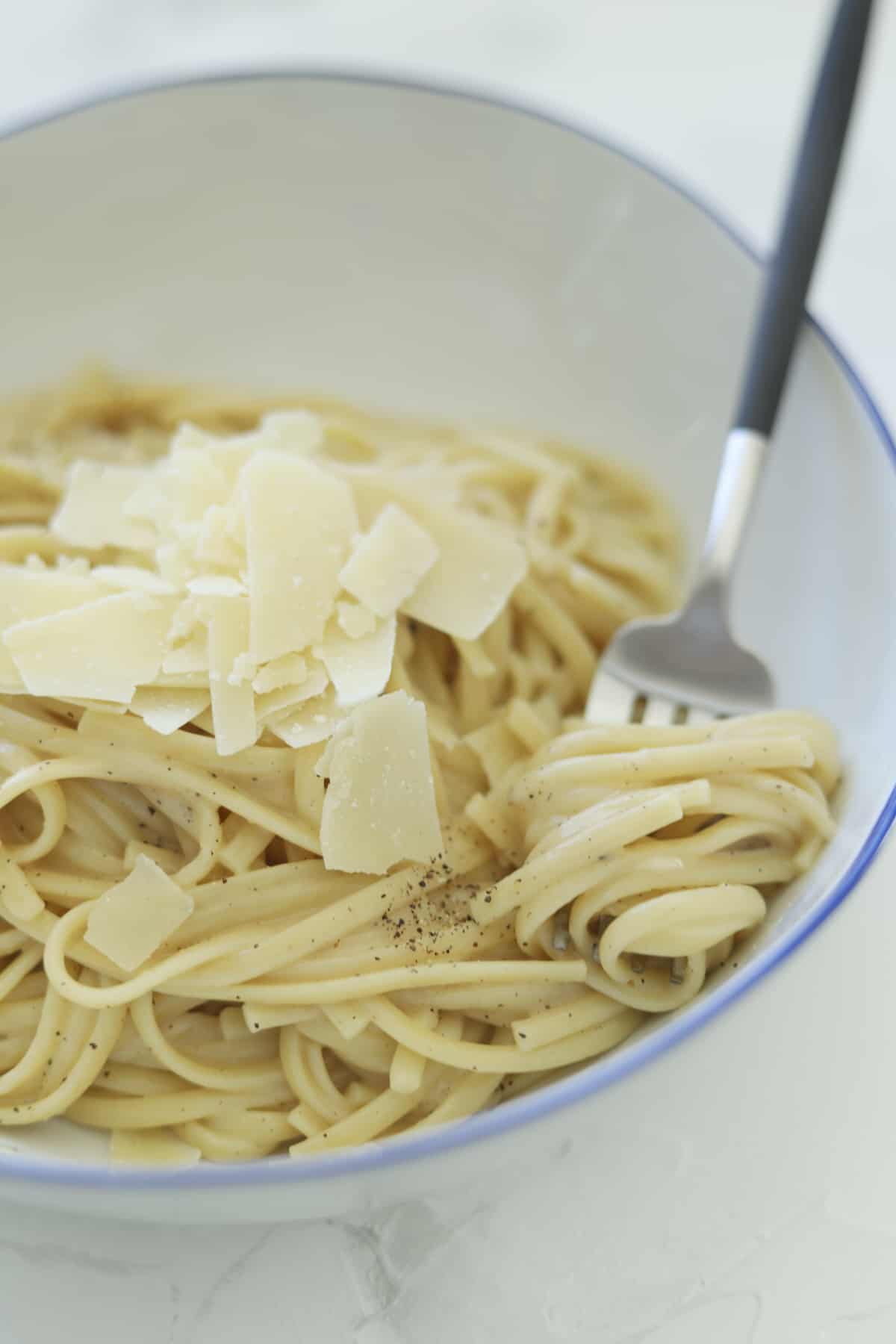 a fork twirling a bite of cacio e pepe in a bowl of pasta topped with Parmesan flakes