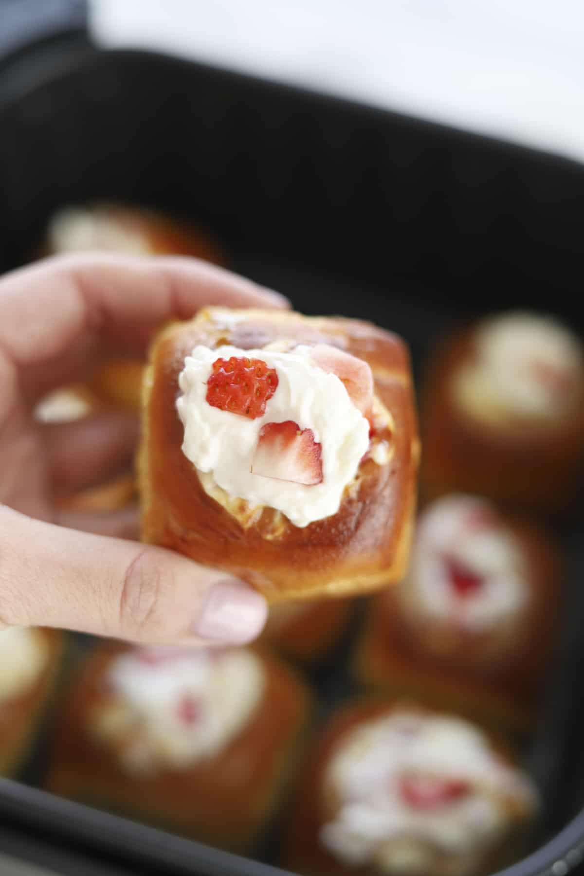 a hand holding an air fried strawberry cream cheese stuffed Hawaiian roll 