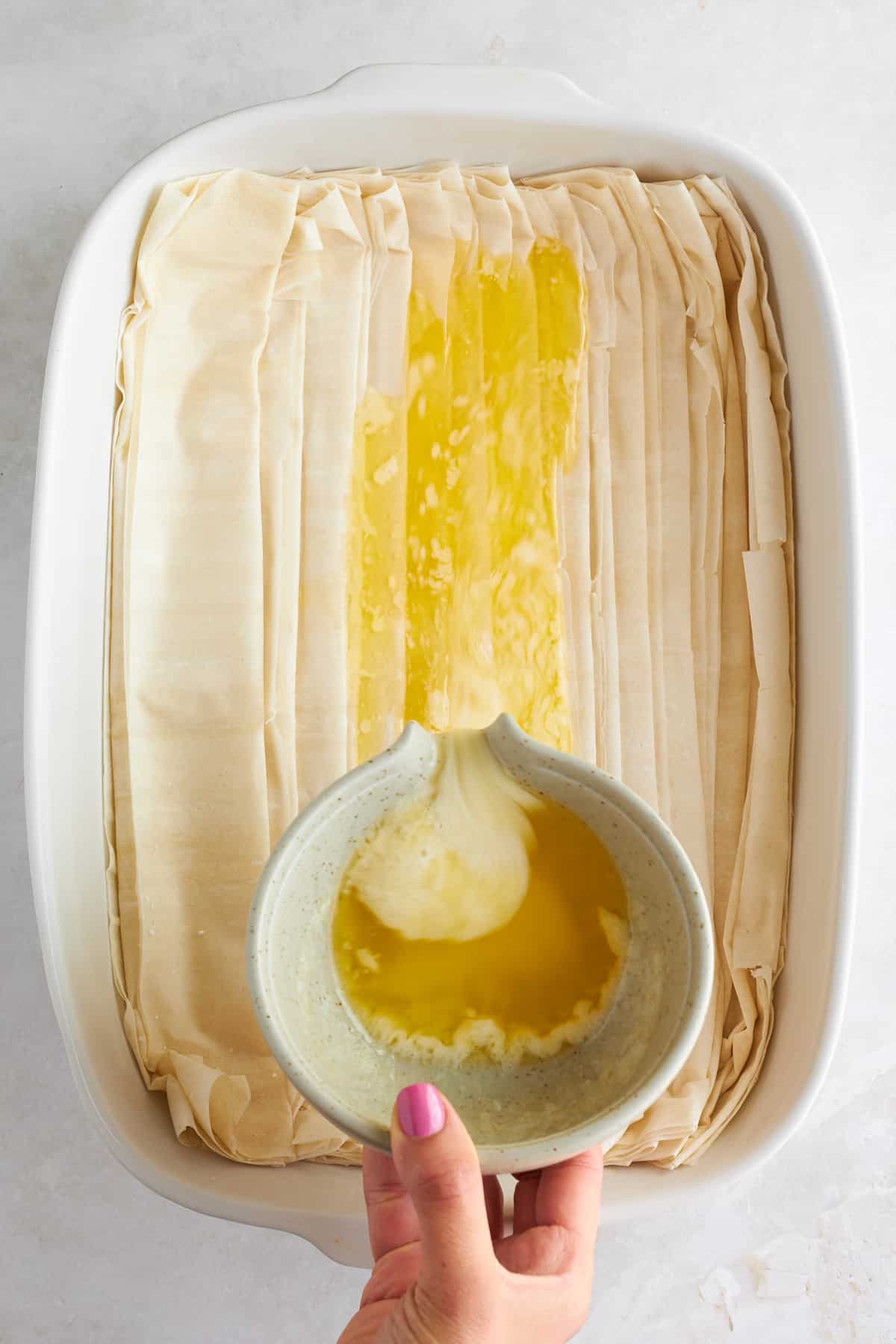 Melted butter being poured over crinkled phyllo dough in a baking dish.