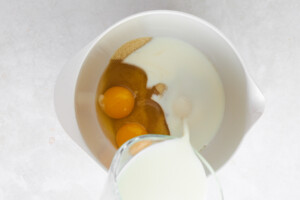Eggs, milk, and sugar being combined in a bowl.